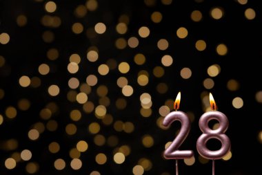 Odaklanamayan ışıklarla arka planı gösteren güzel bir görüntü bir bokeh etkisi yaratarak neşeli ve neşeli bir atmosfer yaratıyor. Bir köşede, iki tane yanan doğum günü mumu biraz sıcaklık ve kutlama katar, özel bir şeyi temsil etmek için mükemmeldir.