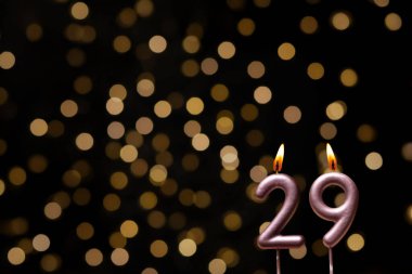 Odaklanamayan ışıklarla arka planı gösteren güzel bir görüntü bir bokeh etkisi yaratarak neşeli ve neşeli bir atmosfer yaratıyor. Bir köşede, iki tane yanan doğum günü mumu biraz sıcaklık ve kutlama katar, özel bir şeyi temsil etmek için mükemmeldir.