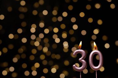 Odaklanamayan ışıklarla arka planı gösteren güzel bir görüntü bir bokeh etkisi yaratarak neşeli ve neşeli bir atmosfer yaratıyor. Bir köşede, iki tane yanan doğum günü mumu biraz sıcaklık ve kutlama katar, özel bir şeyi temsil etmek için mükemmeldir.