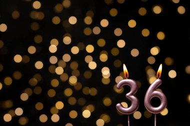 Odaklanamayan ışıklarla arka planı gösteren güzel bir görüntü bir bokeh etkisi yaratarak neşeli ve neşeli bir atmosfer yaratıyor. Bir köşede, iki tane yanan doğum günü mumu biraz sıcaklık ve kutlama katar, özel bir şeyi temsil etmek için mükemmeldir.