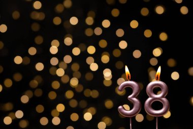 Odaklanamayan ışıklarla arka planı gösteren güzel bir görüntü bir bokeh etkisi yaratarak neşeli ve neşeli bir atmosfer yaratıyor. Bir köşede, iki tane yanan doğum günü mumu biraz sıcaklık ve kutlama katar, özel bir şeyi temsil etmek için mükemmeldir.