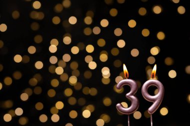 Odaklanamayan ışıklarla arka planı gösteren güzel bir görüntü bir bokeh etkisi yaratarak neşeli ve neşeli bir atmosfer yaratıyor. Bir köşede, iki tane yanan doğum günü mumu biraz sıcaklık ve kutlama katar, özel bir şeyi temsil etmek için mükemmeldir.