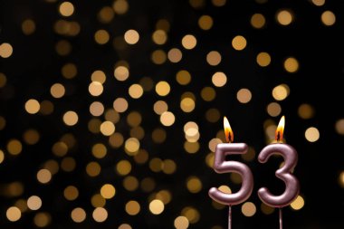 Odaklanamayan ışıklarla arka planı gösteren güzel bir görüntü bir bokeh etkisi yaratarak neşeli ve neşeli bir atmosfer yaratıyor. Bir köşede, iki tane yanan doğum günü mumu biraz sıcaklık ve kutlama katar, özel bir şeyi temsil etmek için mükemmeldir.