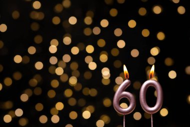 Odaklanamayan ışıklarla arka planı gösteren güzel bir görüntü bir bokeh etkisi yaratarak neşeli ve neşeli bir atmosfer yaratıyor. Bir köşede, iki tane yanan doğum günü mumu biraz sıcaklık ve kutlama katar, özel bir şeyi temsil etmek için mükemmeldir.