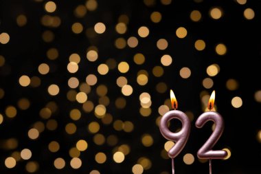 Odaklanamayan ışıklarla arka planı gösteren güzel bir görüntü bir bokeh etkisi yaratarak neşeli ve neşeli bir atmosfer yaratıyor. Bir köşede, iki tane yanan doğum günü mumu biraz sıcaklık ve kutlama katar, özel bir şeyi temsil etmek için mükemmeldir.