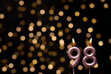 Odaklanamayan ışıklarla arka planı gösteren güzel bir görüntü bir bokeh etkisi yaratarak neşeli ve neşeli bir atmosfer yaratıyor. Bir köşede, iki tane yanan doğum günü mumu biraz sıcaklık ve kutlama katar, özel bir şeyi temsil etmek için mükemmeldir.