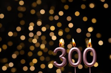 Odaklanamayan ışıklarla arka planı gösteren güzel bir görüntü bir bokeh etkisi yaratarak neşeli ve neşeli bir atmosfer yaratıyor. Bir köşede, iki tane yanan doğum günü mumu biraz sıcaklık ve kutlama katar, özel bir şeyi temsil etmek için mükemmeldir.