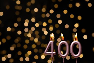 Odaklanamayan ışıklarla arka planı gösteren güzel bir görüntü bir bokeh etkisi yaratarak neşeli ve neşeli bir atmosfer yaratıyor. Bir köşede, iki tane yanan doğum günü mumu biraz sıcaklık ve kutlama katar, özel bir şeyi temsil etmek için mükemmeldir.