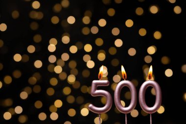 Odaklanamayan ışıklarla arka planı gösteren güzel bir görüntü bir bokeh etkisi yaratarak neşeli ve neşeli bir atmosfer yaratıyor. Bir köşede, iki tane yanan doğum günü mumu biraz sıcaklık ve kutlama katar, özel bir şeyi temsil etmek için mükemmeldir.