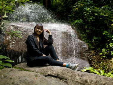 Young lady in long dress and brown boots sitting on stones, on the background of rocks and lake in autumn countryside, fashion stylish woman