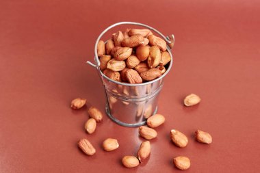 A small metal bucket filled with raw peanuts on a brown background. clipart