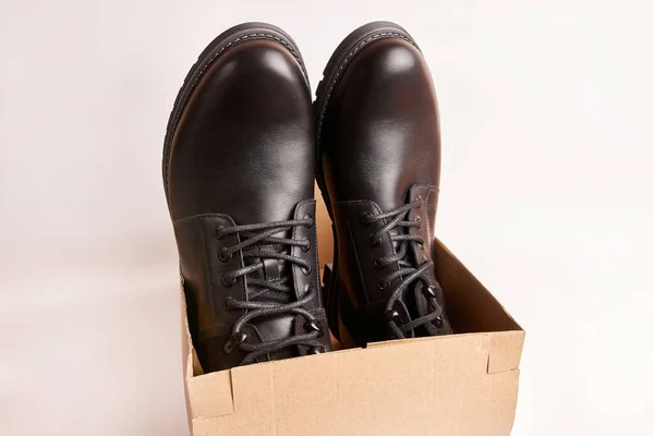 Black leather men\'s boots in a box on a white background. Buying warm shoes for the winter.