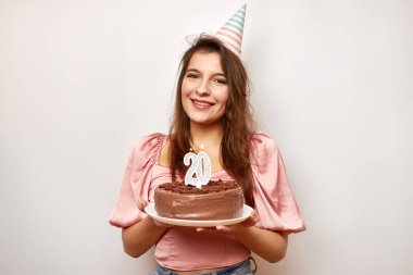 Kız elinde 20 numara şeklinde mumlu şenlikli bir pasta tutuyor. Doğum günü kutlaması konsepti.
