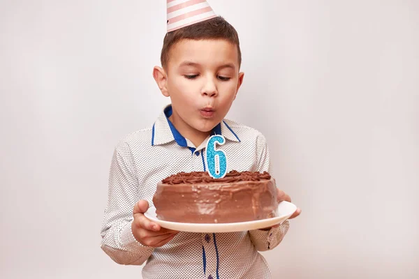 A boy is holding a birthday cake and blowing out a candle in the form of the number 6. Birthday celebration concept.