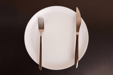 Siyah arka planda çatal ve bıçaklı beyaz tabak..