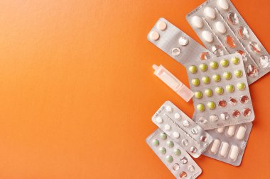 Packets with various pills and a container with liquid on an orange background.