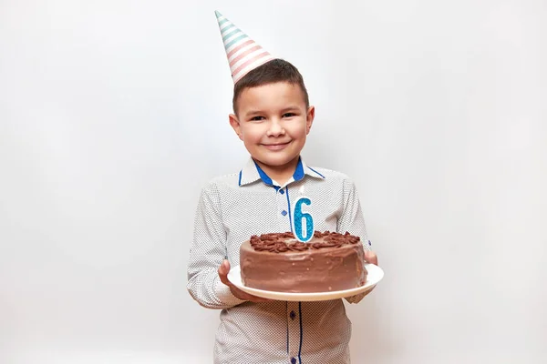 Cheerful boy holding a birthday cake with a candle in the form of number 6. Birthday celebration concept.