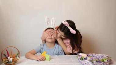 The girl covers her brother's eyes and makes an Easter surprise for him. Celebrating Easter in the family. Easter games and fun.