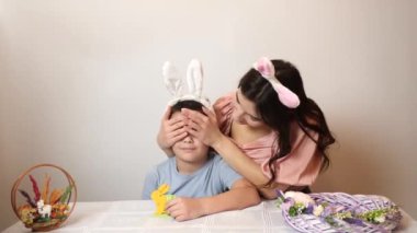 The girl covers her brother's eyes and makes an Easter surprise for him. Celebrating Easter in the family. Easter games and fun.