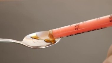 With the help of a dispenser, the medicine is poured into a spoon.