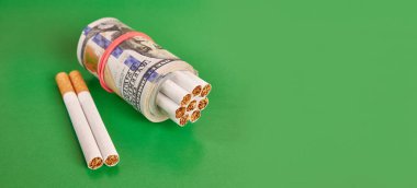 Yeşil arka planda 100 dolarlık banknotlara sarılı sigaralar. Pahalı sigara kavramı.