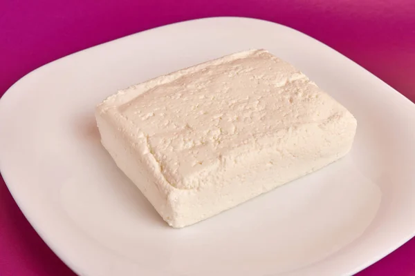 stock image A slice of sour milk cheese on a white plate.