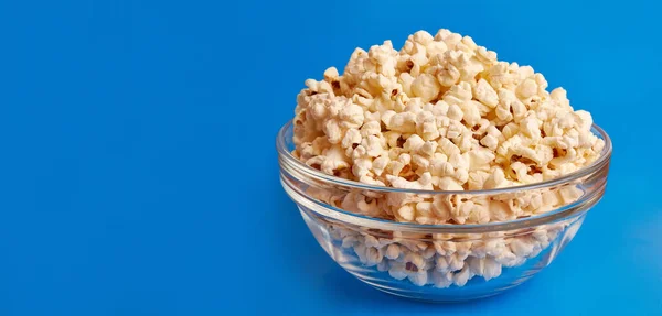 A sweet, tasty snack. A bowl on a blue background is completely filled with popcorn.