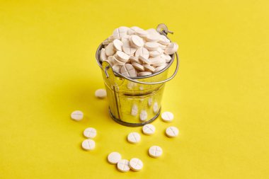 Sarı arka planda haplarla dolu küçük metal bir kova. Uyuşturucu kullanımı ve aşırı doz.