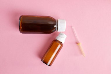 Tıbbi grafik geçmişi. İki şişe sıvı ilaç ve pembe arka planda bir pipet..