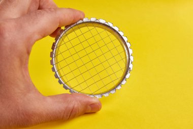 Metal bir manuel sebze kesicisi sarı arka planda elde tutulur..