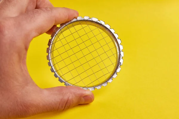 Metal bir manuel sebze kesicisi sarı arka planda elde tutulur..