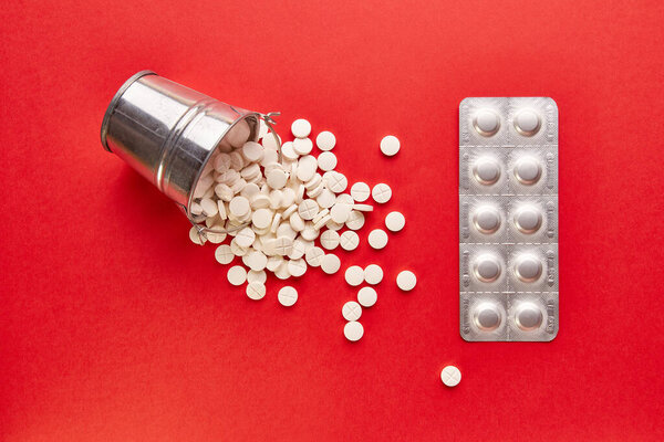 A small metal bucket filled with pills on a red background. Concept of drug abuse and overdose.