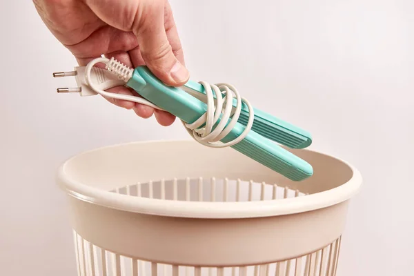 A broken hair curler is thrown into the trash. Disposal and recycling of waste.