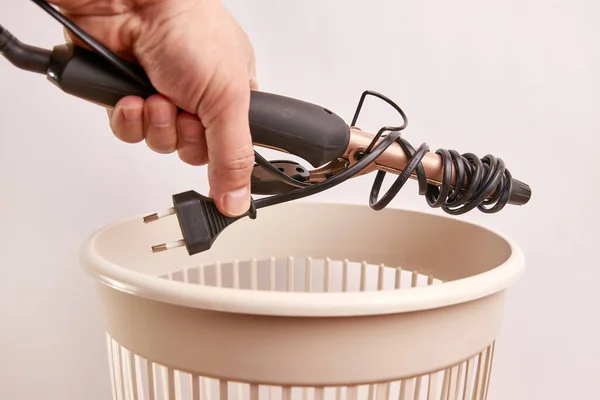 A broken hair curler is thrown into the trash. Disposal and recycling of waste.