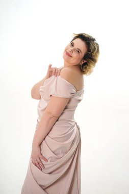 Bej elbiseli, gülümseyen bir kadın beyaz arka planda poz verir..