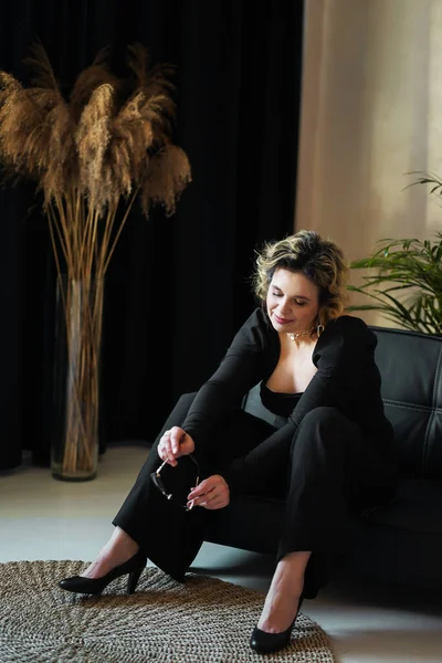 stock image A smiling woman in a black suit sits holding glasses.