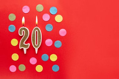 Kırmızı arka planda, renkli konfetiyle 20 numara. Mutlu doğum günü mumları. Doğum günü, yıldönümü, önemli randevu, tatil kavramı. Uzayı kopyala Pankart