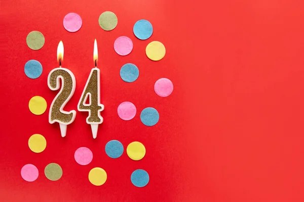 Number 24 on a red background with colored confetti. Happy birthday candles. The concept of celebrating a birthday, anniversary, important date, holiday. Copy space. banner