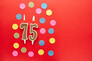 Renkli konfetiyle kırmızı arka planda 75 numara. Mutlu doğum günü mumları. Doğum günü, yıldönümü, önemli randevu, tatil kavramı. Uzayı kopyala Pankart