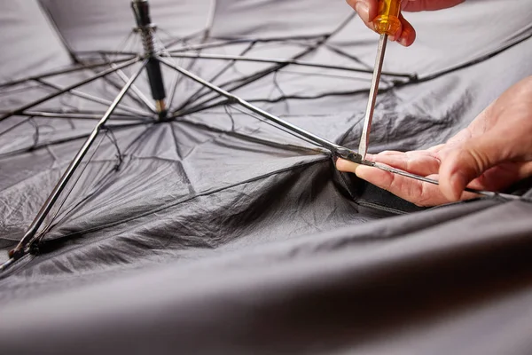 A craftsman repairs an umbrella by changing the needle with a hand tool. Small repair of household items.