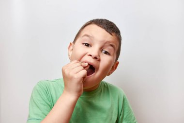 6-7 yaşlarında yakışıklı bir çocuk parmağıyla bebek dişini sallamaya çalışıyor..