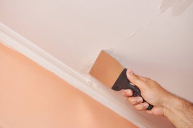 Tavandan eski boya kalıntılarını bir spatulayla soy. İnşaat çalışmaları.
