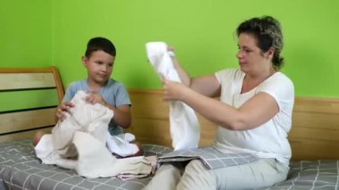 Çocuk neşeyle annesinin giysileri katlamasına yardım eder. Ev ödevi. Yıkama, ütüleme ve katlama.