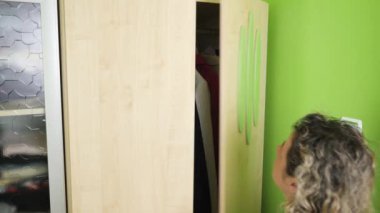 Kadın dolabı açar ve elbiselerini çıkarır..