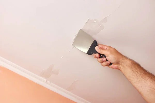 Peel off the remains of old paint from the ceiling with a spatula. Construction works.
