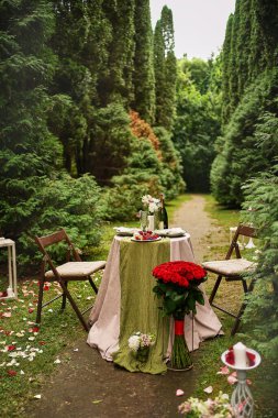 Ormanın ortasındaki çimenlikte şölen masası. Evlilik teklifi sırasında romantik ve şenlikli bir ortam..                                 