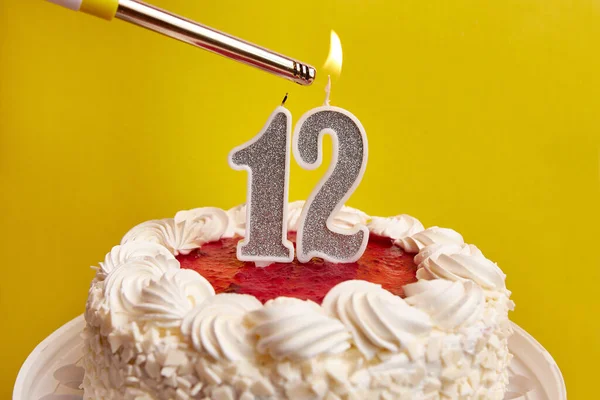 A candle in the form of the number 12, stuck in a festive cake, is lit. Celebrating a birthday or a landmark event. The climax of the celebration.