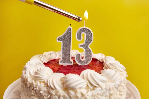 A candle in the form of the number 13, stuck in a festive cake, is lit. Celebrating a birthday or a landmark event. The climax of the celebration.