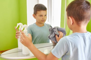 Çocuk aynayı bez ve deterjanla yıkıyor. Ev ödevi. Ev temizliği.