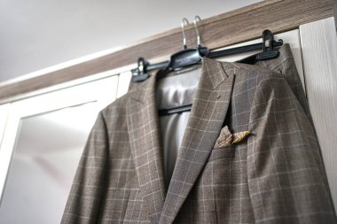 Gri takım elbiseli şık bir adam odadaki askıda asılı duruyor..                                    